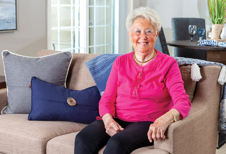A smiling resident sitting on a couch wearing a pink shirt.
