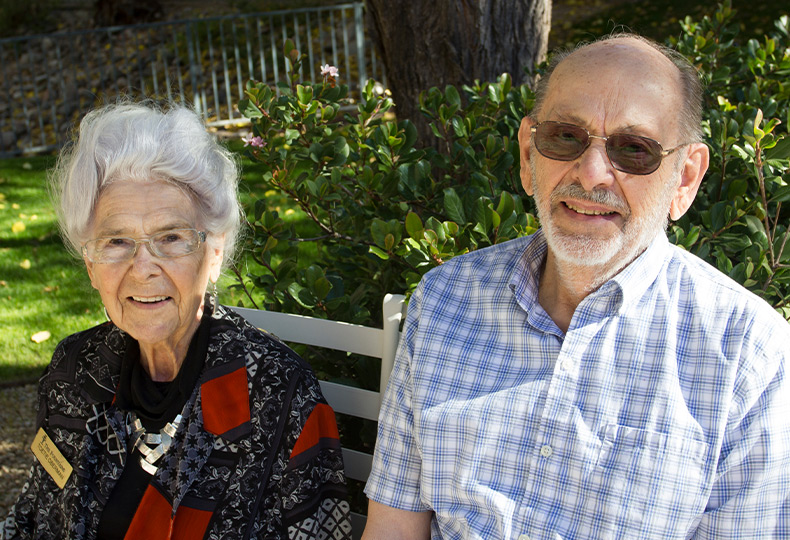 Residents smiling while sitting on a park bench.