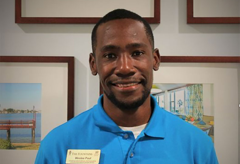 Weslee, a Watermark associate, is standing in front of a wall of framed photos. smiling
