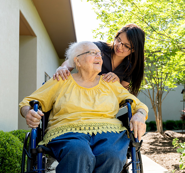 A caregiver smiling with a resident out in the garden.