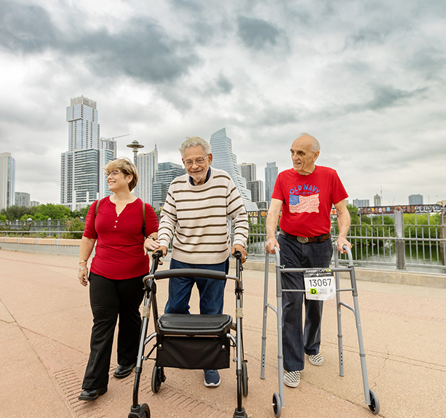 Two residents walking with a caregiver with a cityscape behind them.