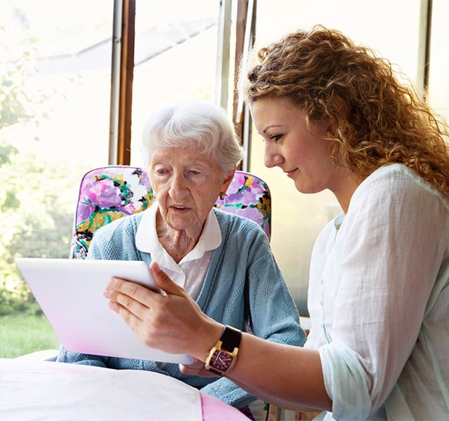 A caregiver is helping a resident use a tablet.