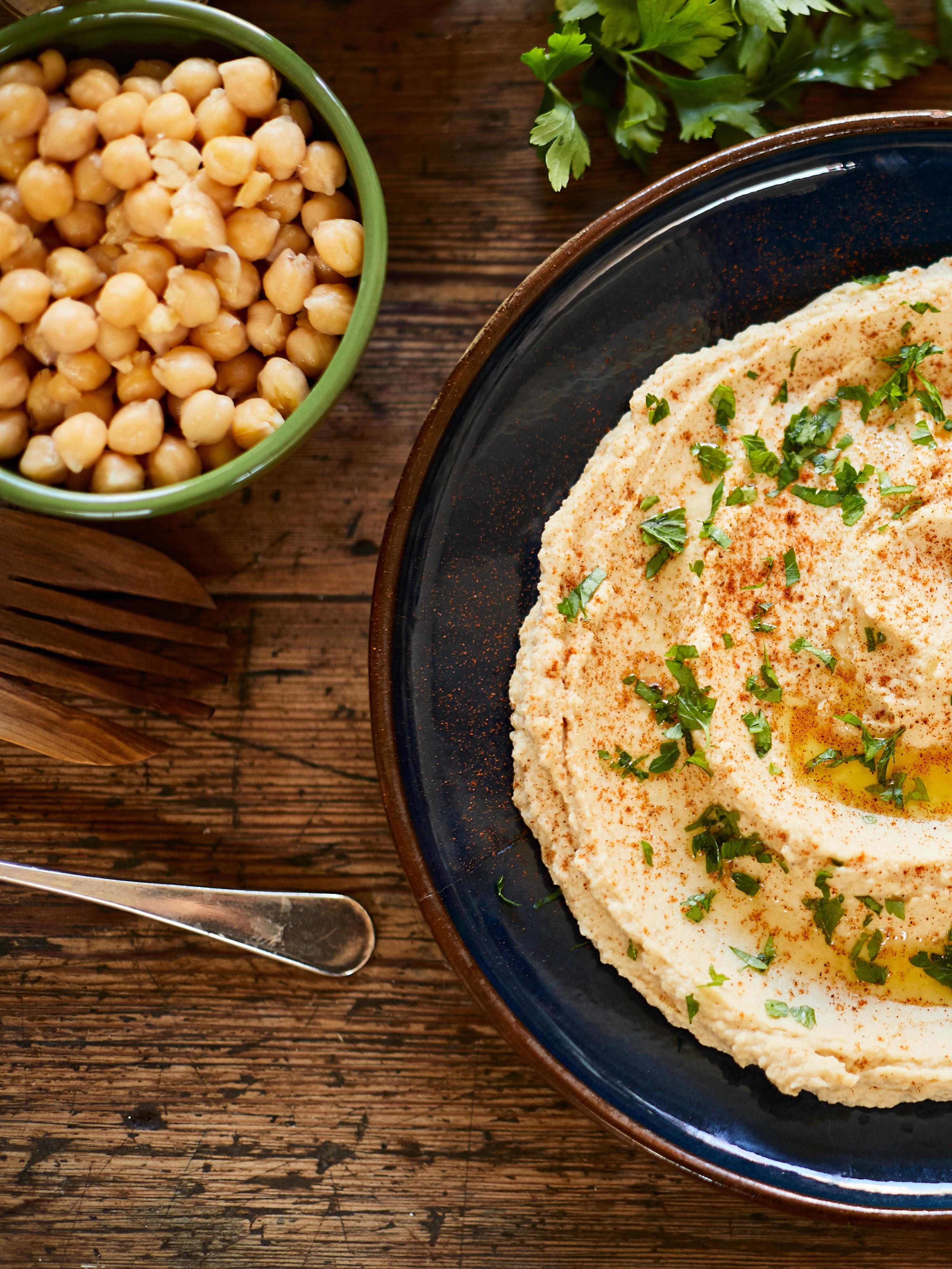 A bowl of hummus next to a bowl of chickpeas.