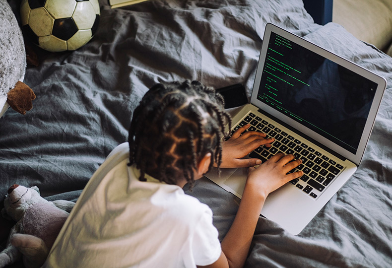 A child laying on the bed with a computer.