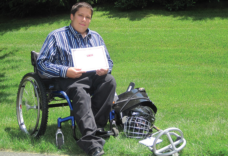A teen sitting in a wheel chair with their sled hockey equipment.