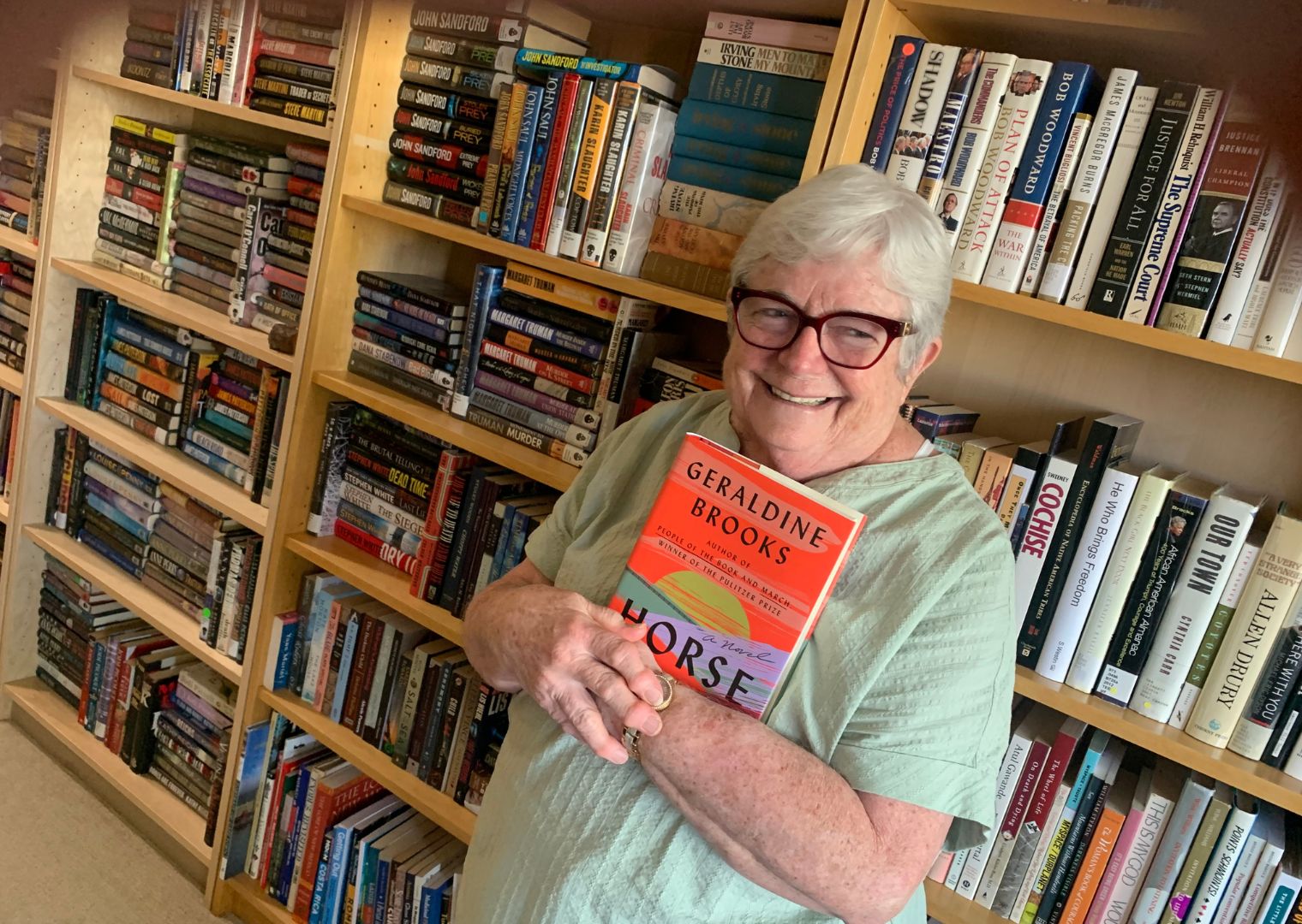 Phyllis Woman holding book in front of bookcase.