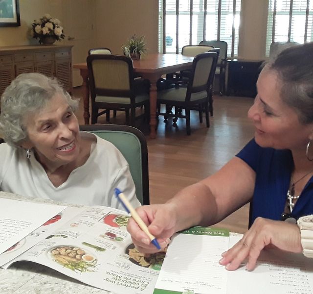 Janet-Associate Resident and associate sitting at table writing a grocery list.