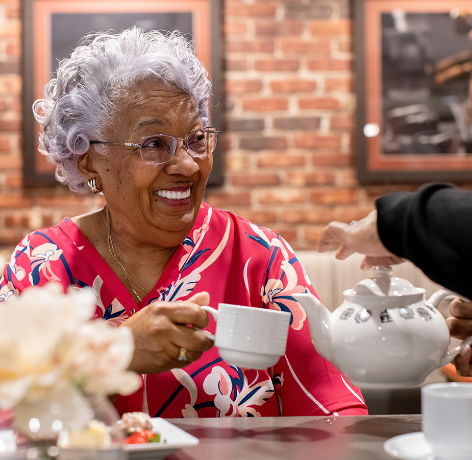 A resident at a table having tea poured in her cup.